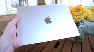 MacBook Air 13 M3 held closed in a hand above a slatted wooden table